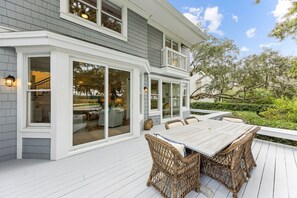 Une maison dotée d’un patio couvert, de grandes fenêtres et d’un coin repas aménagé avec des meubles en osier.
