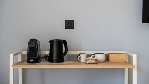 Eine Küchenzeile mit Kaffeemaschine, Wasserkocher und einem kleinen Schrank mit Tassen und Teekanne.