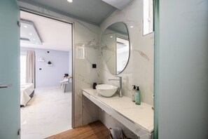 A modern bathroom with a marble vanity, a large mirror, and a white sink. - The Stone Suite | Avra Suites (Kos)