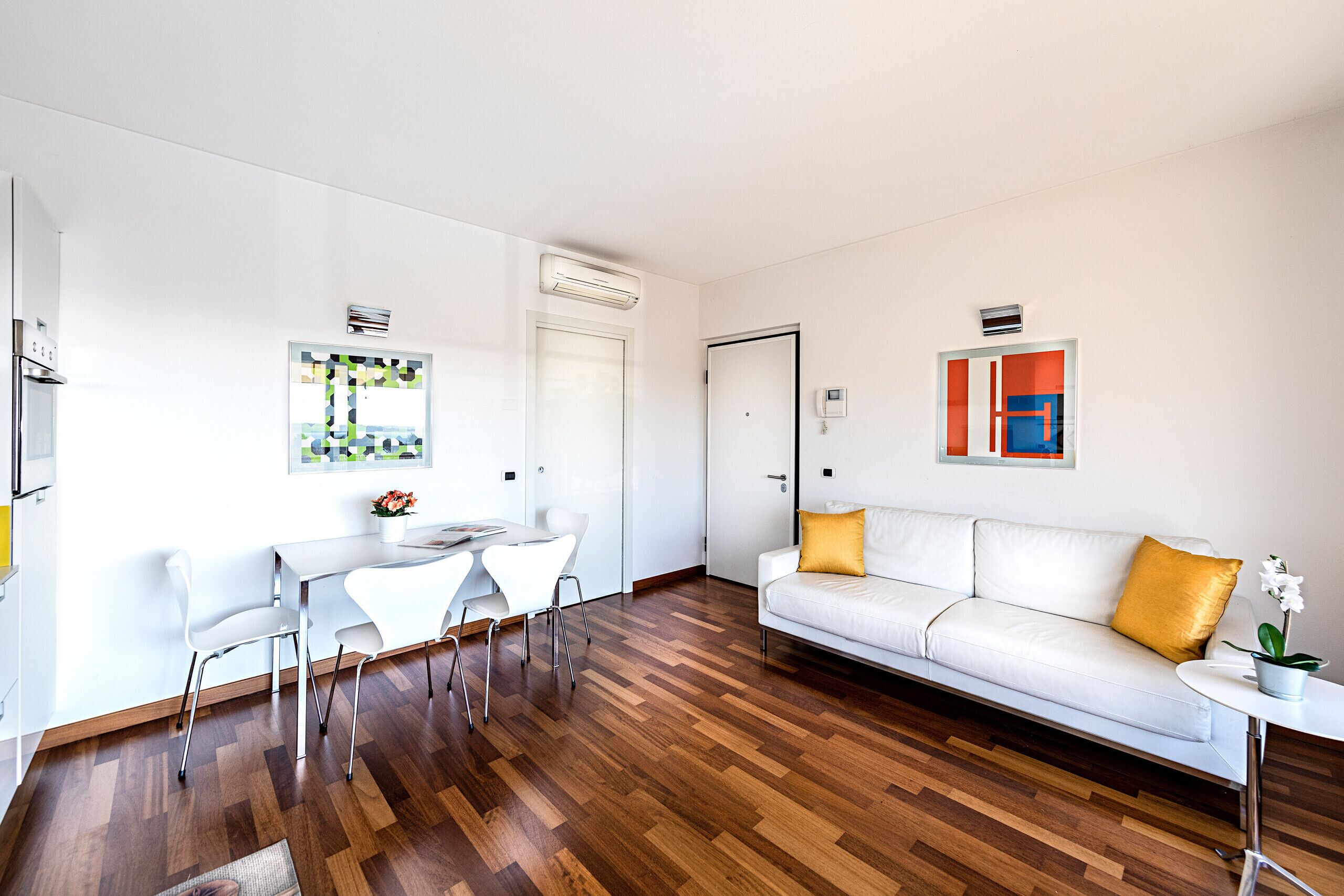 A modern living room with a white sofa, a dining table with chairs, and a small side table with a plant.