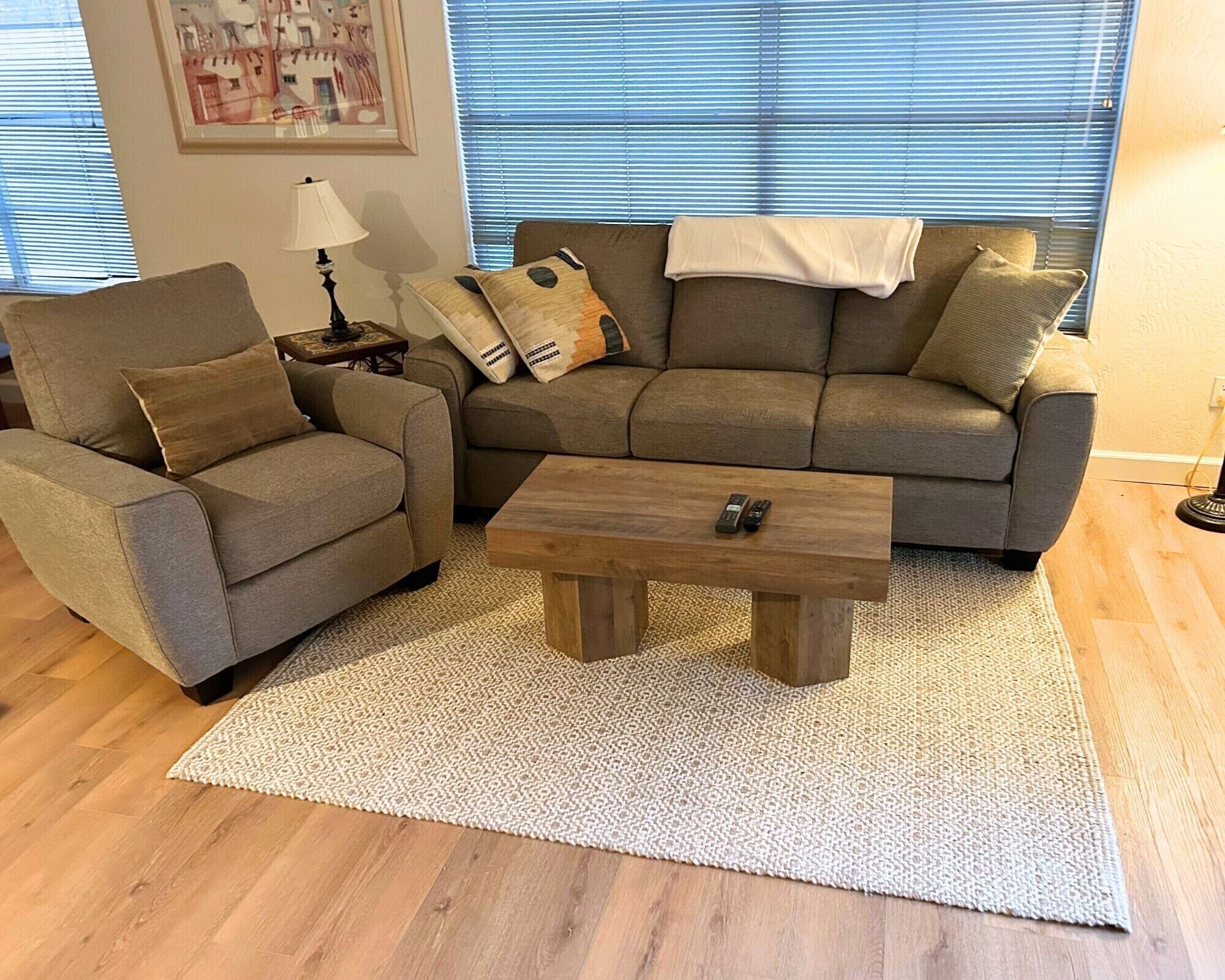 A living room with a sofa, armchair, and coffee table, a lamp, and a patterned rug.