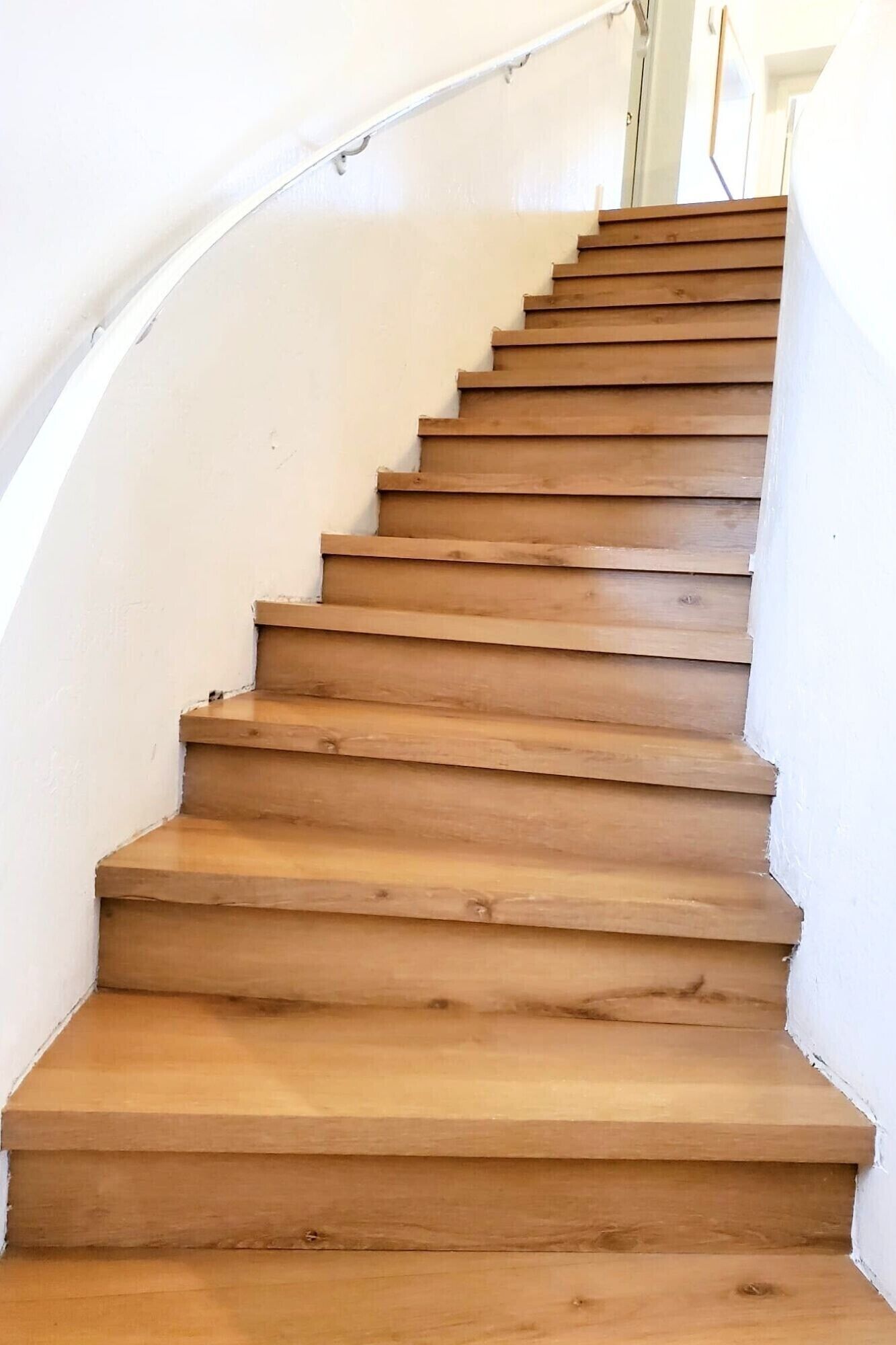 A wooden staircase with white walls and a curved handrail.