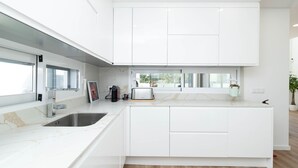 A modern kitchen with white cabinetry, a built-in island, a sink, and a window overlooking a garden. - Dino Beach House - Three Bedroom House, Sleeps 6 (Aroeira)