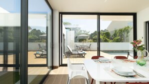 A modern outdoor dining area with a pool, sliding glass doors, and a view of the surrounding landscape. - Dino Beach House - Three Bedroom House, Sleeps 6 (Aroeira)