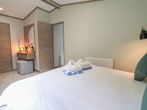 A hotel room with a bed, a bedside table with a lamp, a mirror, and a radiator. - Cedar Lodge 2 Bedrooms With hot tub (Northwich)