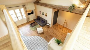 A loft-style room with exposed wooden beams, a sofa, a coffee table, and a hanging light fixture. - Apartment "Origan" (Saint-Rémy-de-Provence)