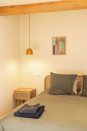 Quarto com cama, luminária pendente, mesa de cabeceira de madeira e quadro na parede.