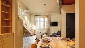A dining area with a wooden table set for four, a staircase, a sofa, and a television on the wall. - Apartment "Origan" (Saint-Rémy-de-Provence)