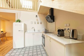 Cozinha compacta com geladeira, pia e fogão, área de jantar com cadeiras e escada para um andar superior.