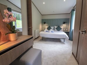 A bedroom with a bed, bedside tables, a potted plant, a window, and a door. - Cedar Lodge 3 Bedrooms With hot tub (Northwich)