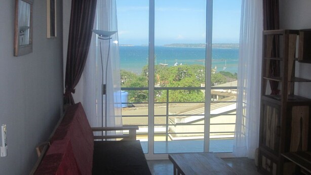 A room with a large sliding glass door leading to a balcony with a view of the sea and greenery. - Superb apartment with sea view, right in the center of town (Antsiranana)