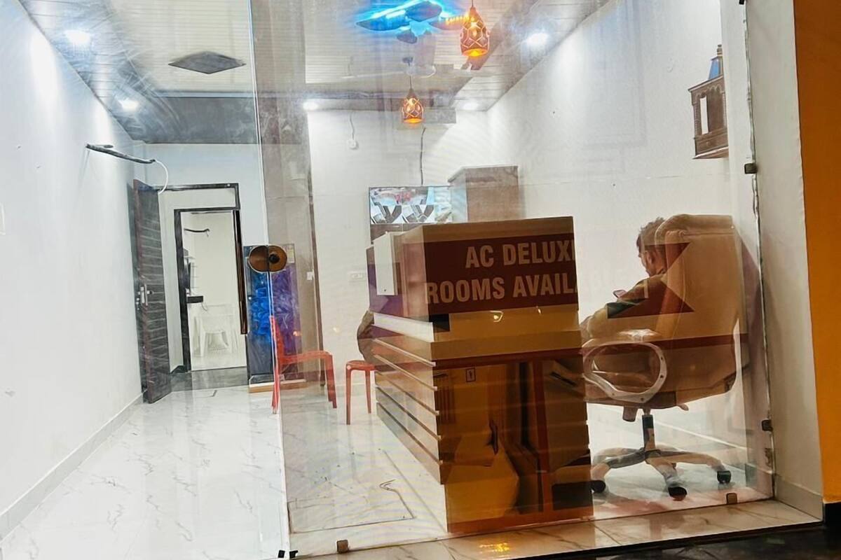 A hotel room with a glass partition, a sign indicating 'AC DELUXE ROOMS AVAILABLE', and a 'Welcome' sign above the entrance.