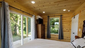 Un dormitorio de cabaña de madera con una cama grande, un televisor sobre un mueble de madera y un ventanal corredero que da a un balcón.