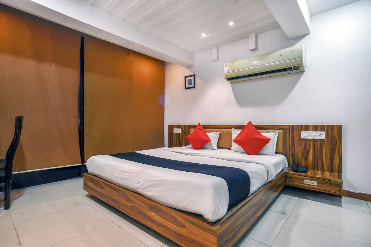 Una cama bien hecha con cabecera de madera, una mesita de noche con un teléfono y un equipo de aire acondicionado montado en la pared.