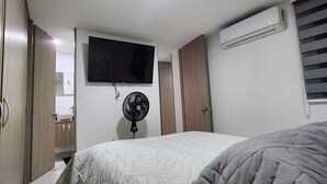 A bedroom with a bed, a TV mounted on the wall, a standing fan, and an air conditioning unit. - Mirador Baluarte Pool& Parking (Cartagena de Indias)