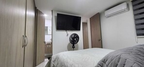 A bedroom with a bed, a TV mounted on the wall, a standing fan, and an air conditioning unit. - Mirador Baluarte Pool& Parking (Cartagena de Indias)
