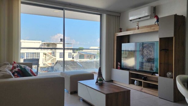 A modern living room with a large window, a flat-screen TV, a sofa, and a coffee table. - Mirador Baluarte Pool& Parking (Cartagena de Indias)