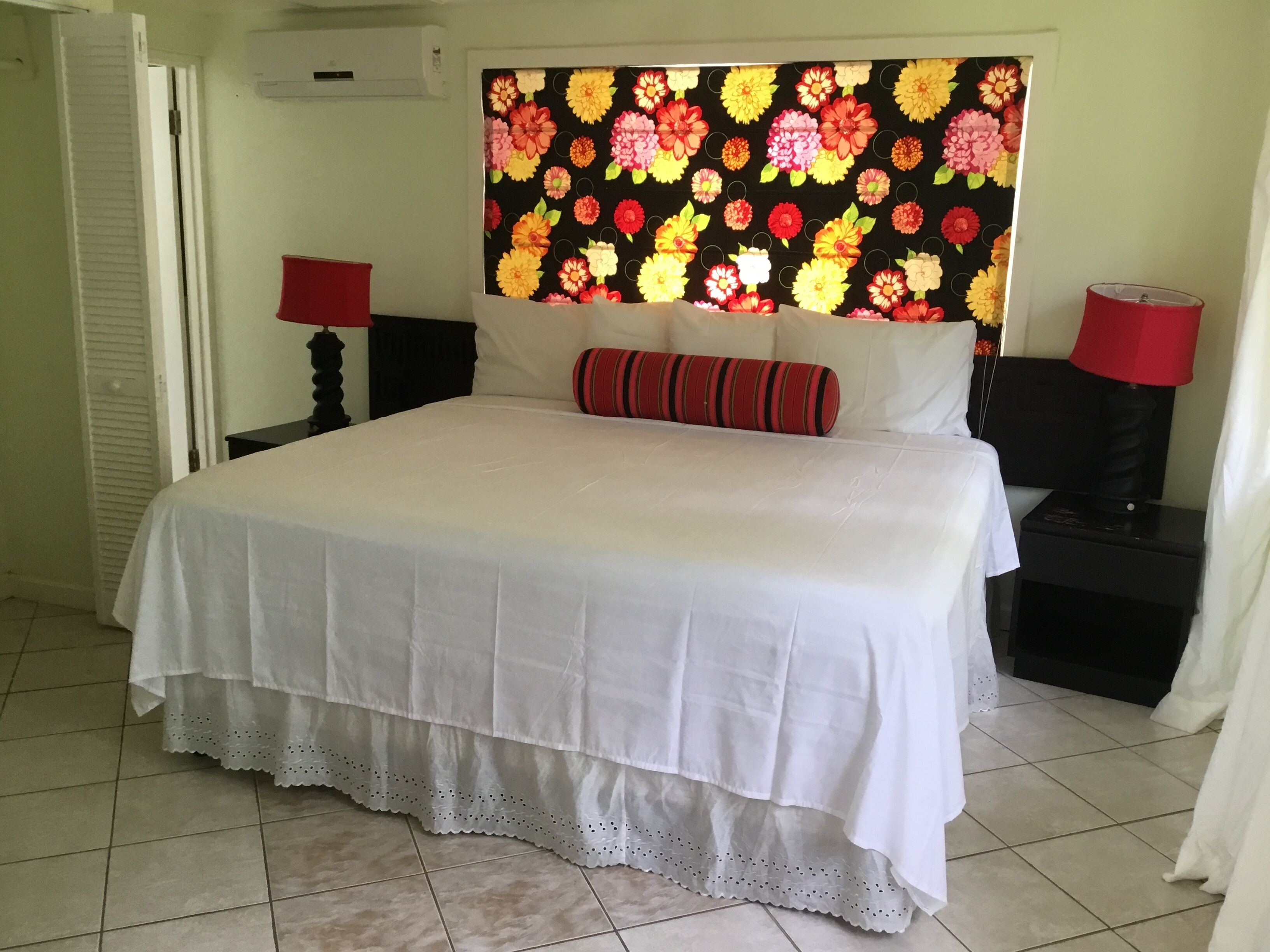A neatly made bed with a white bedspread and a decorative pillow, a floral-patterned headboard, and two bedside tables with red lamps.