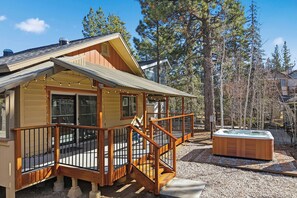 Une cabane en bois dotée d’une terrasse, d’un bain à remous et offrant une vue sur les arbres environnants.