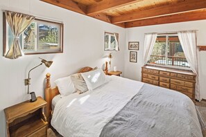 Une chambre à coucher avec un lit en bois, une table de chevet avec une lampe, une commode et une fenêtre avec des rideaux.