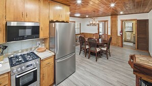 Eine Küche mit Holzschränken, einem Edelstahlkühlschrank, einem Gasherd und einem Essbereich mit Holztisch und Stühlen.