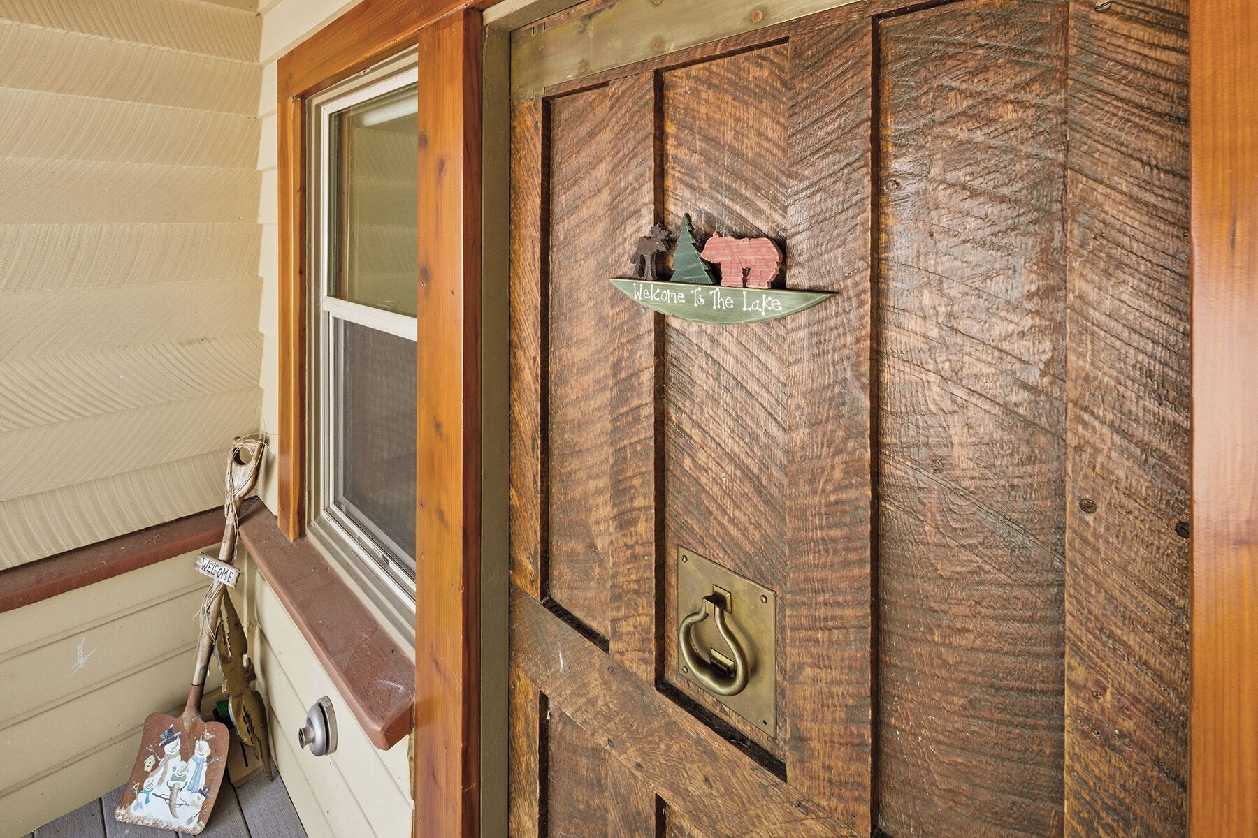 Una puerta de madera con diseño rústico, una ventana y un cartel de bienvenida.
