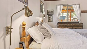 Ein Schlafzimmer mit einem hölzernen Bett, einem Nachttisch mit Lampe, einer Kommode und einem Fenster mit Vorhängen.