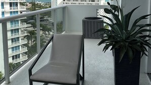 En balkon med en liggestol, en potteplante og udsigt over havet og bygninger.