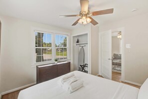 A bedroom with a bed, a ceiling fan, a window with blinds, a dresser, and a door leading to another room. - The Emerson Bungalow Private Retreat Near Park (North Charleston)