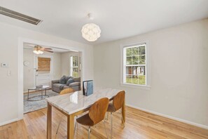A dining area with a marble table and wooden chairs, a ceiling fan, and a window with blinds. - The Emerson Bungalow Private Retreat Near Park (North Charleston)
