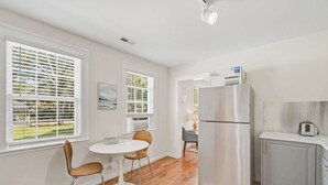 Eine moderne Küche mit einem Edelstahl-Kühlschrank, einer kleinen Essecke mit zwei Stühlen und einem Fenster mit Jalousien.