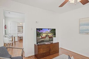 A room with a television on a wooden dresser, a dining table with chairs, and a painting on the wall.