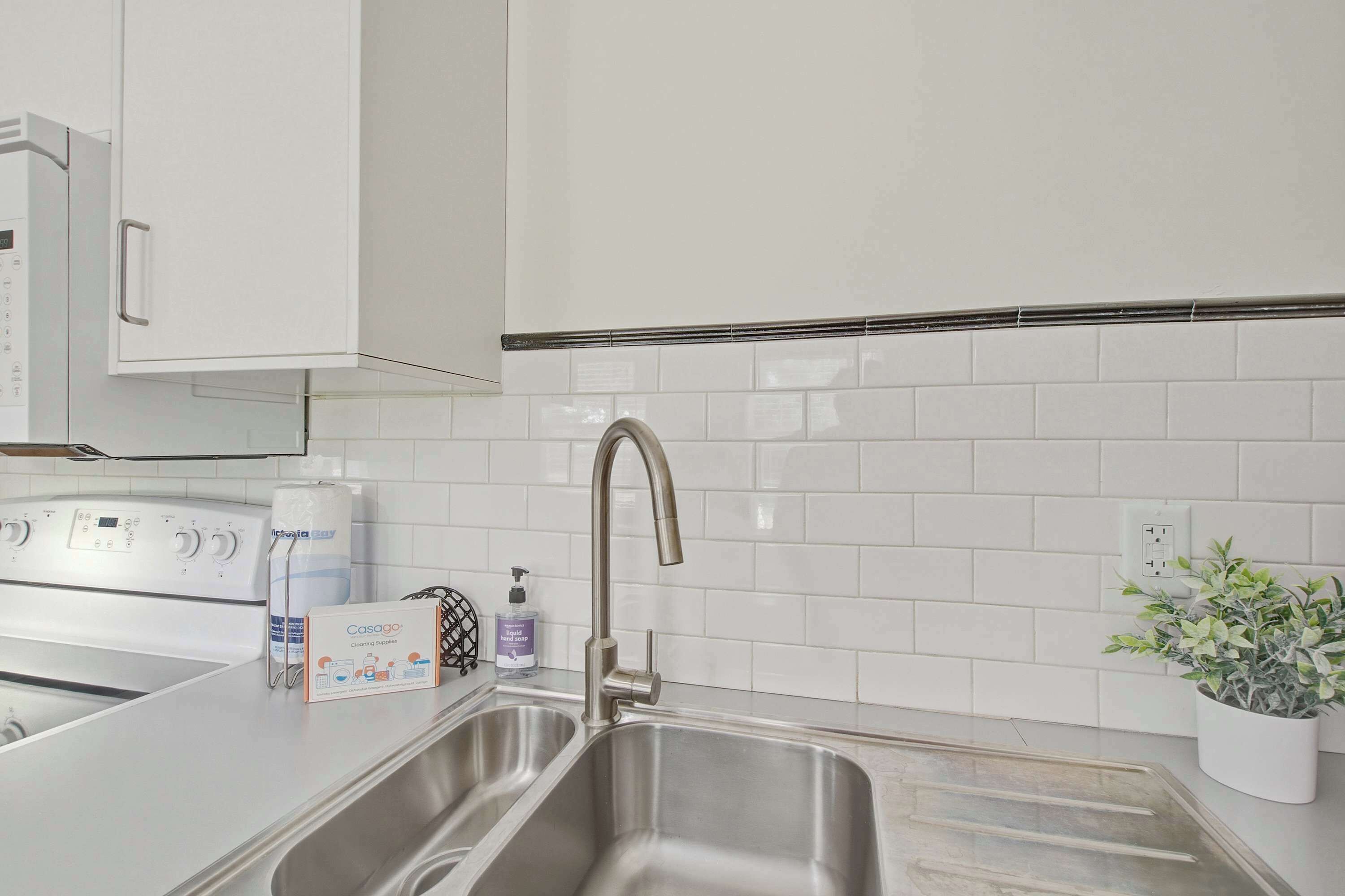 A modern kitchen with a stainless steel sink, a built-in oven, and a white tiled backsplash.