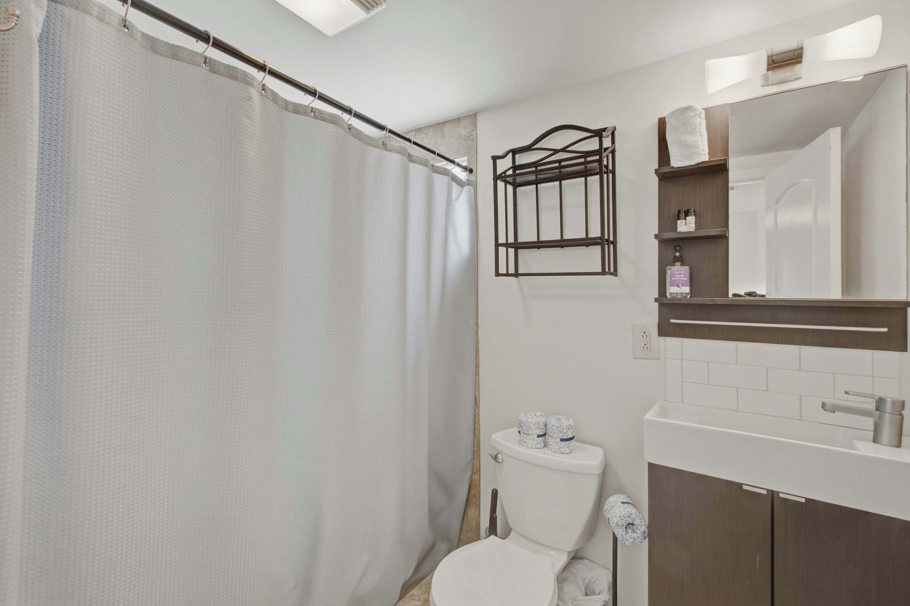 A bathroom with a shower curtain, a toilet, a shelf with toiletries, and a mirror.