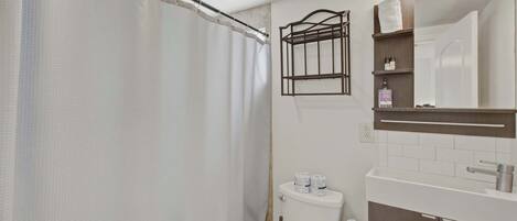 A bathroom with a shower curtain, a toilet, a shelf with toiletries, and a mirror.