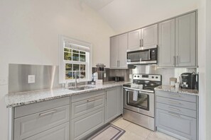 A modern kitchen with grey cabinets, stainless steel appliances, a window, and a granite countertop. - Stylish Bungalow Stay Near Downtown Charleston (North Charleston)