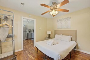 A hotel room with a bed, a ceiling fan, a painting, and a kitchenette in the background. - Quiet Retreat Near Downtown Charleston (North Charleston)