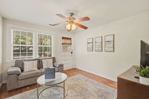 A living room with a ceiling fan, a sofa, a coffee table, and a TV. - Quiet Retreat Near Downtown Charleston (North Charleston)
