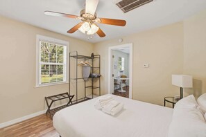 A bedroom with a bed, a ceiling fan, a window with blinds, a drying rack, and a door leading to another room. - Quiet Retreat Near Downtown Charleston (North Charleston)