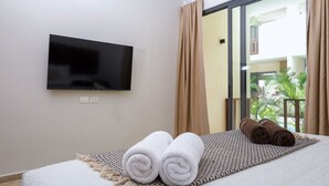Ein Hotelzimmer mit einem Bett, einem an der Wand befestigten Flachbildfernseher und Blick auf einen Balkon mit Vorhängen.