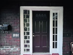 Una puerta de madera oscura con un marco blanco, un buzón con el número 1336 y una pared de ladrillo.