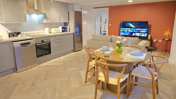A modern kitchen with stainless steel appliances, a dining area with a round table and wooden chairs, and a living room with a sofa and a flat-screen TV. - Stylish and spacious, lower ground floor apartment -Pass the Keys (Shrewsbury)