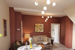 Een woonkamer met een bank, een eettafel gedekt met borden en glazen, een lamp en een decoratieve vaas.