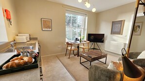 Una sala de estar moderna con comedor, una cocina con lavaplatos y tostadora, y un televisor sobre un mueble.
