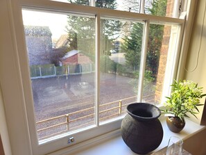 Ein Fenster mit Blick auf einen Parkplatz und ein Gebäude. Auf dem Fensterbrett steht ein Blumentopf.