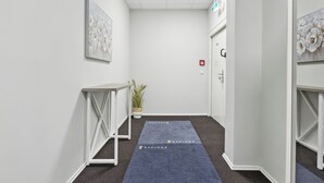 A hallway with white walls, a blue carpet with text, a potted plant, and a door with a fire alarm. - HanseStay Wandsbek (Hamburg)