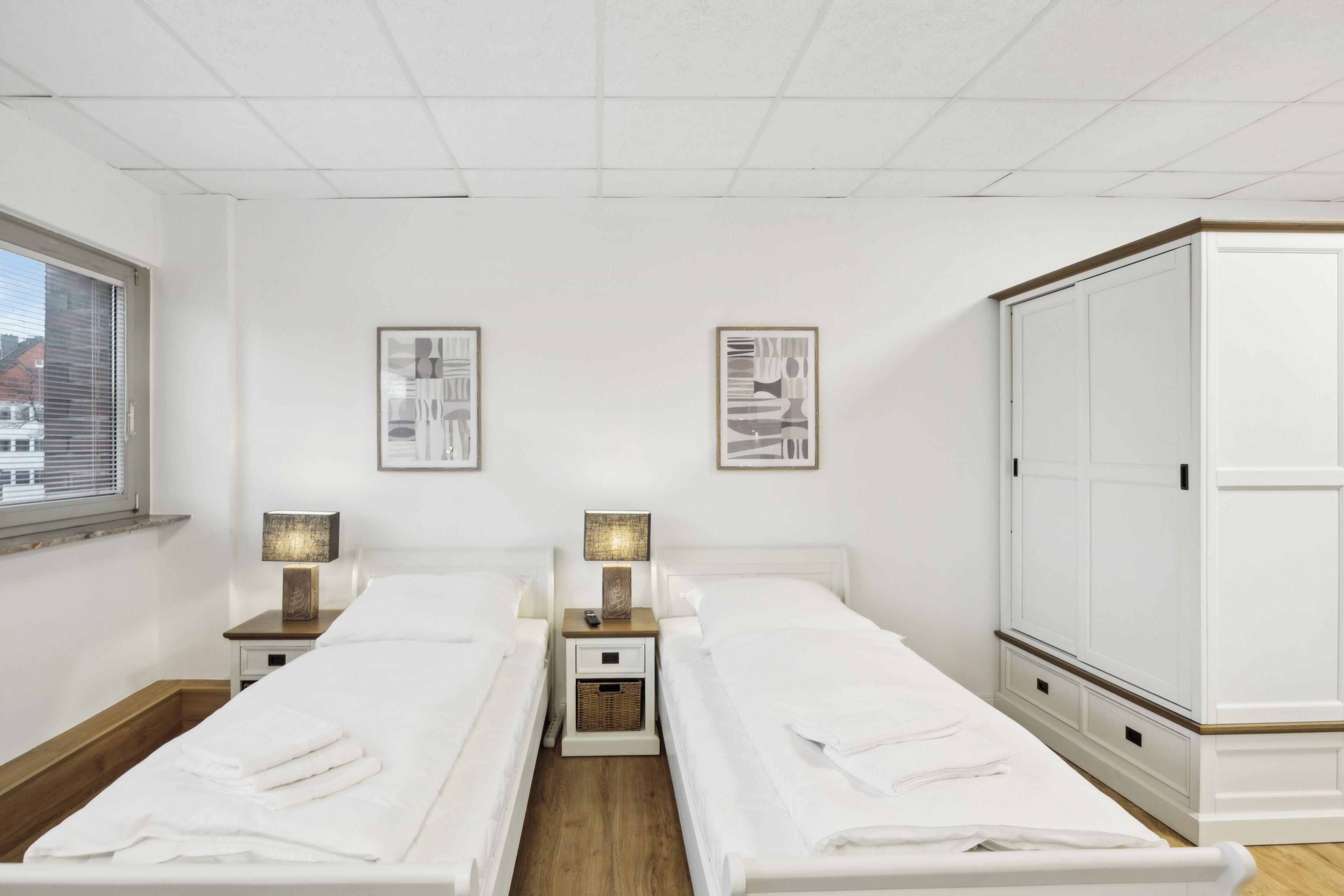 Ein Doppelzimmer mit zwei Betten, Nachttischen, Lampen, gerahmten Bildern und einem Kleiderschrank.