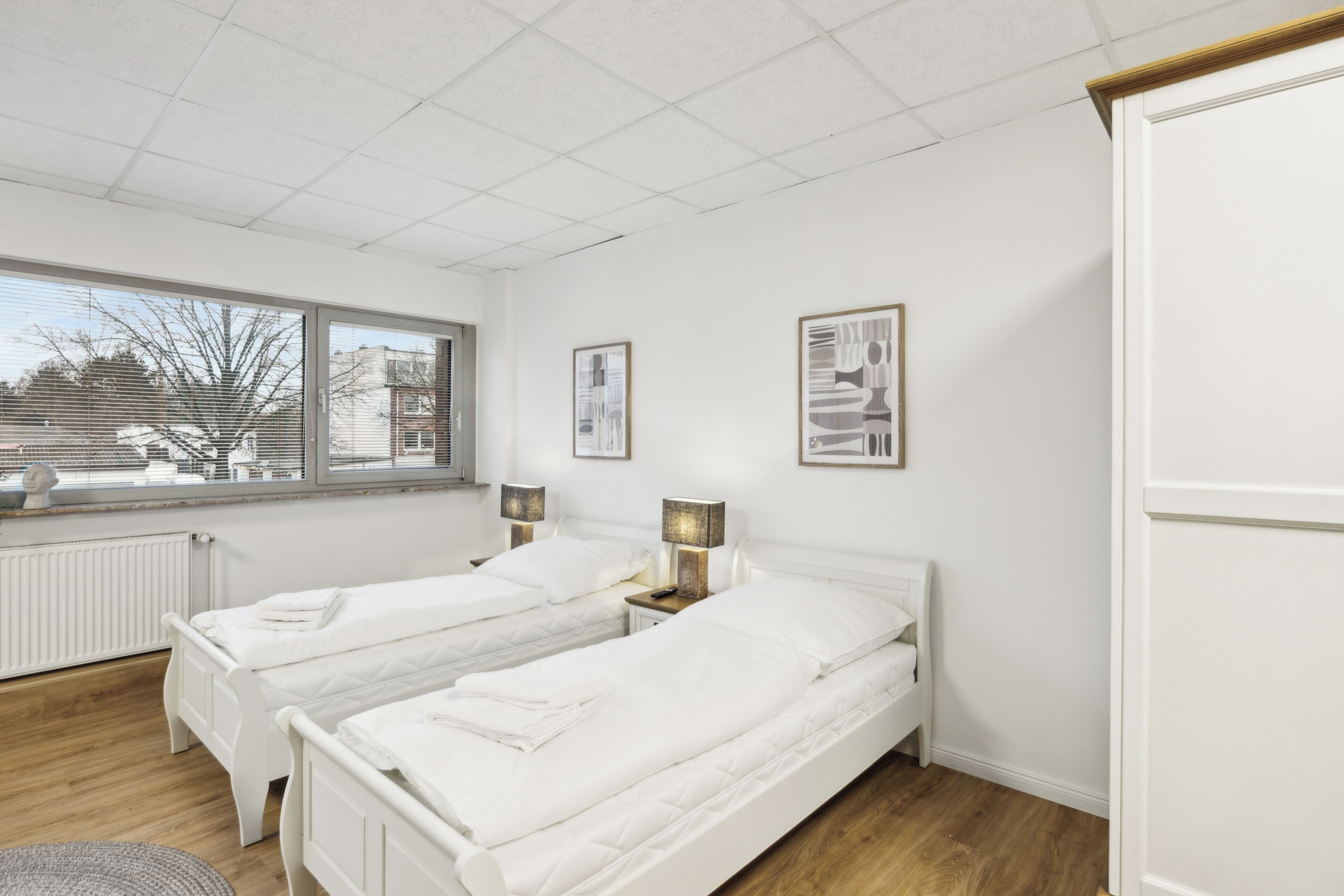 A hotel room with two single beds, a large window, and a radiator.