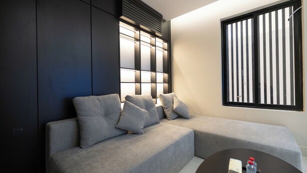 A modern living room with a grey sectional sofa, a small round coffee table, and a large window with vertical blinds. - Luxury two bedroom Apartment Al Rawdha (Riyadh)