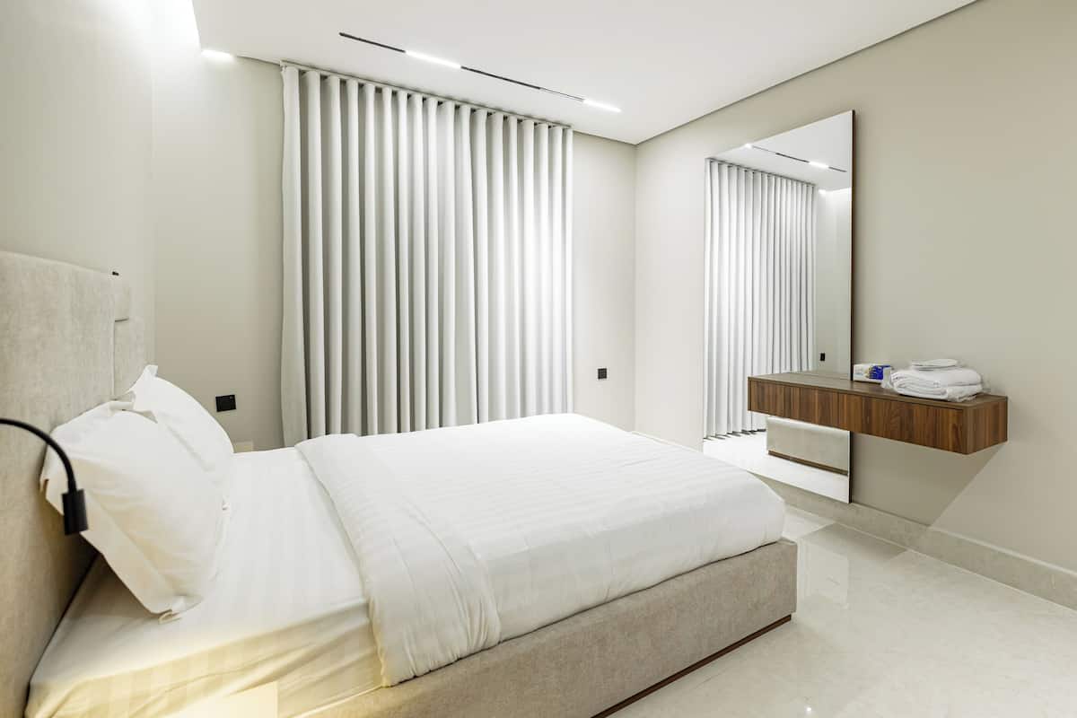 Une chambre moderne comprenant un lit, une table de chevet, un miroir et une étagère intégrée où sont rangées des serviettes.